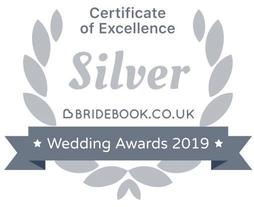 Soft grey laurel leaves surround the words Certificate of Excellence, silver, bridebook.co.uk. A darker grey banner across it says wedding awards 2019.